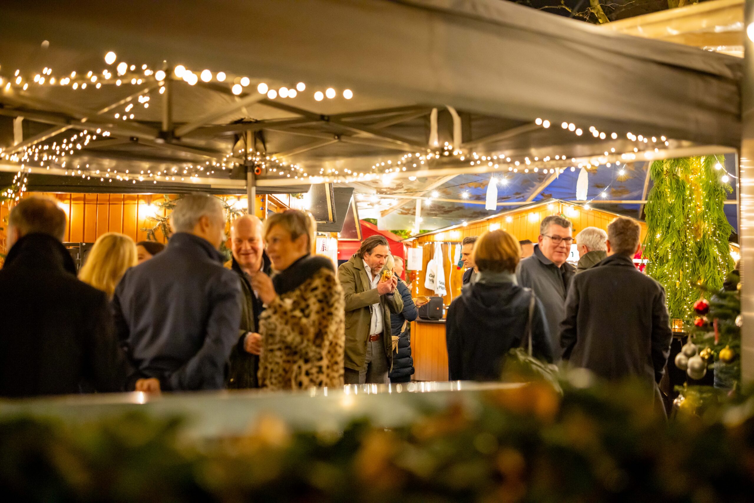 Weihnachtliche Eventfläche des Rotonda Weihnachtsmarkts mit Holzhütten, Gästen und warmem Licht