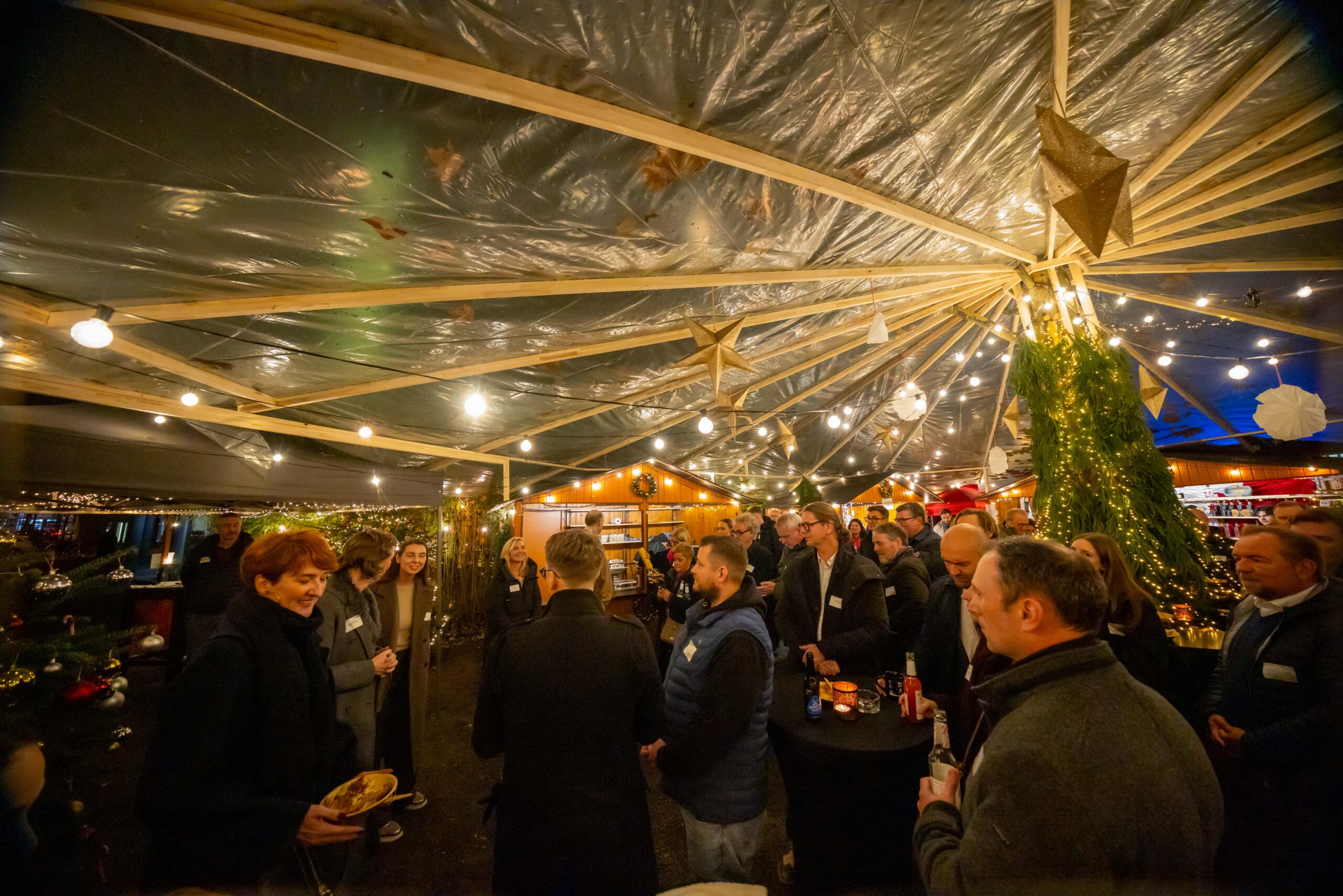 Weihnachtlich beleuchtete Rotonda Eventfläche mit Gästen, Holzhütten und Lichterketten
